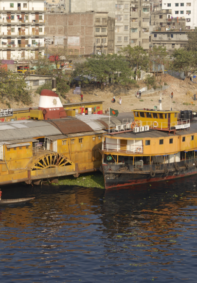 A couple of older steam engine ships on the shore of a city with buildings in the immediate background